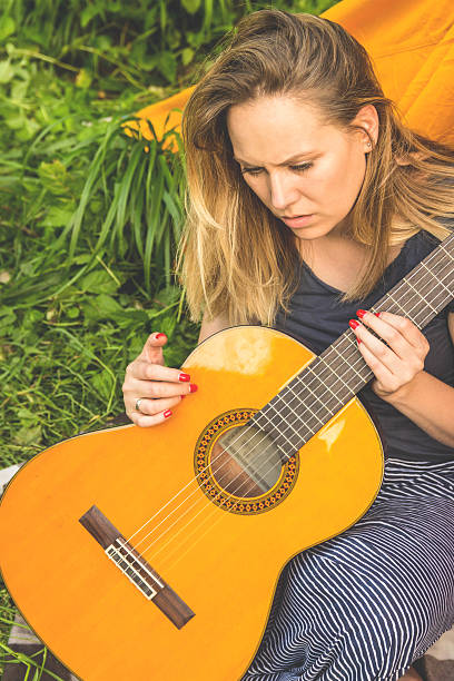 istock young woman sitting on a field and playing guitar 637946236