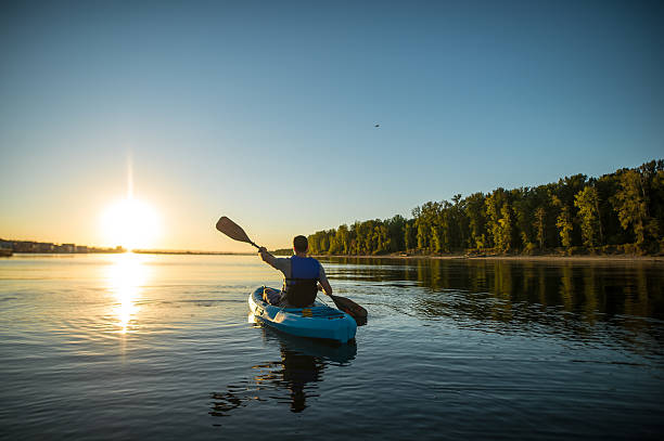 un homme adulte fait du kayak au coucher du soleil sur un paisible - canoe kayak, jaune photos et images de collection