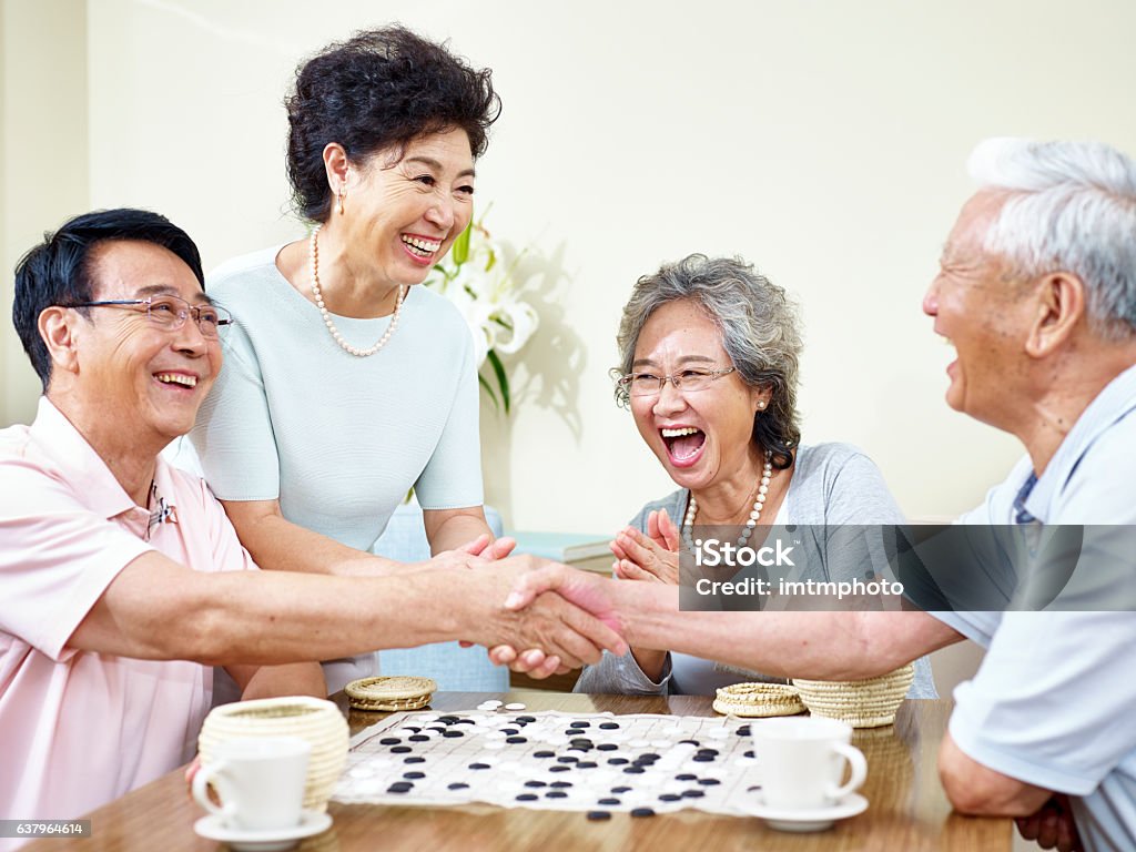 senior asian people playing weiqi senior asian men shaking hands  at the end of a weiqi game. Senior Adult Stock Photo