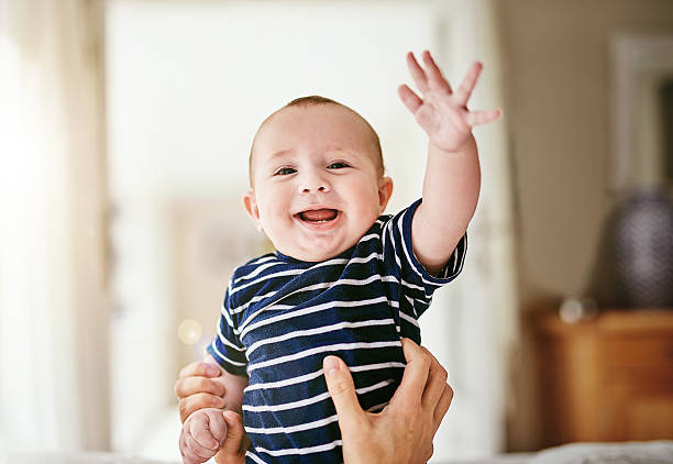 High five! Portrait of an adorable baby boy being held by his unrecognizable mother at home waving stock pictures, royalty-free photos & images