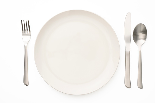 Overhead shot of white plate with table knife, spoon and fork, isolated on white background with clipping path.