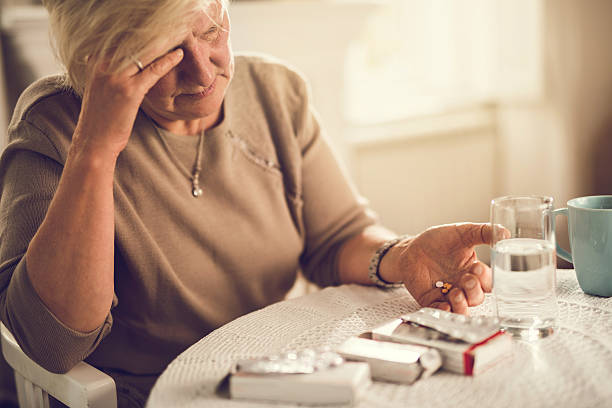 I am going to take a painkiller for my headache! Old woman holding her head in pain while about to take medicines. pill prescription capsule prescription medicine stock pictures, royalty-free photos & images