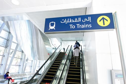 Dubai, UAE - March 24, 2015: To the trains sign. Dubai metro sign. Travellers in background.
