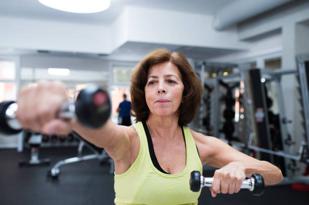 Senior woman in gym working out with weights. Senior woman in sports clothing in gym working out with weights. Close up of hands. senior bodybuilders stock pictures, royalty-free photos & images