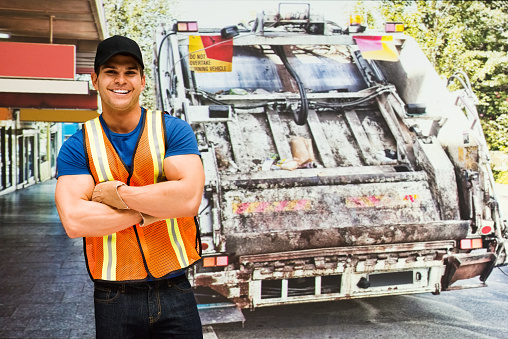 Smiling worker standing in front of garbage can