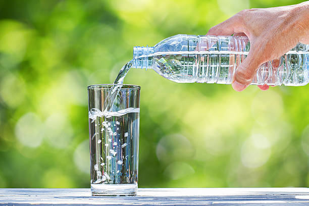 die hand des mannes gießt wasser in glas auf verschwommenen bokeh-hintergrund - destilliertes wasser stock-fotos und bilder