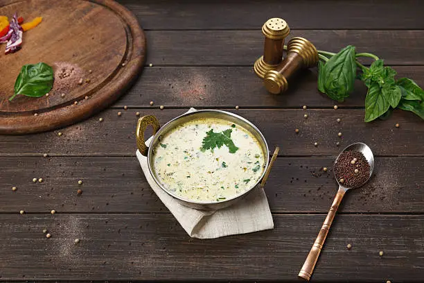 Vegan and vegetarian dish, cold summer yoghurt raita soup in copper bowl. Indian cuisine meal on wooden served table background. Healthy eastern local restaurant food above view
