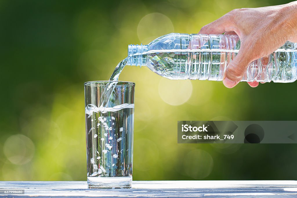 Die Hand des Mannes gießt Wasser in Glas auf verschwommenen Bokeh-Hintergrund - Lizenzfrei Trinken Stock-Foto