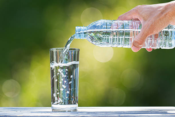 die hand des mannes gießt wasser in glas auf verschwommenen bokeh-hintergrund - drinking water drink men stock-fotos und bilder