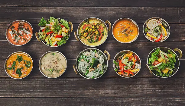 Vegan or vegetarian restaurant dishes top view, hot spicy indian soups, rice and salads in copper bowls. Traditional indian cuisine meal assortment on wood background. Healthy eastern local food