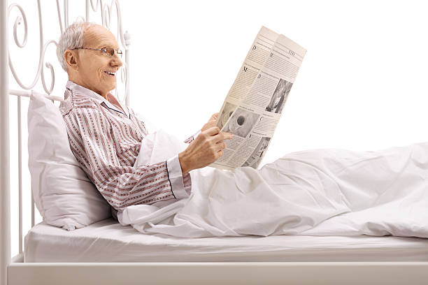 uomo maturo sdraiato a letto e leggendo un giornale - mattress newspaper reading bed foto e immagini stock