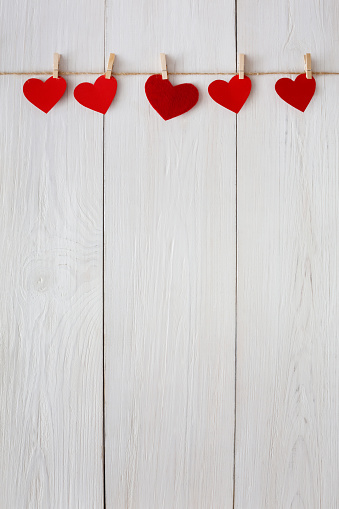 Valentine background with red paper hearts row border on clothespins on white rustic wood planks. Happy lovers day card mockup, copy space