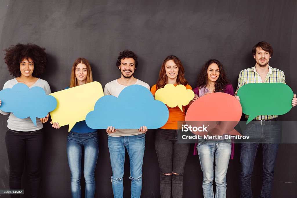 Happy friends holding speech bubbles Group of young people holding speech bubbles against blackboard Breaking the Ice Stock Photo