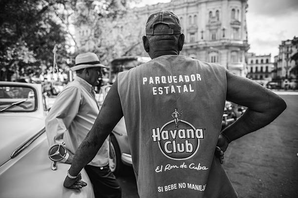 Havana, Cuba - October 14, 2016. Drivers of tourist rides: Old American made cars  parked on square in front of  Capitolio- Cuban Parliament building  in Old Havana, Cuba. Two Drivers  standing beside the car and talking. Other people in the background. One of countless vintage US made cars imported to Cuba before the Revolution but still running after more than 50 years due to ingenuity of Cuban car mechanics and some help of various old car parts, including the left over of Russian diesel engines. These restored cars, looking almost as new are in use now for foreign tourists only, with hourly rate of $25 per hour.