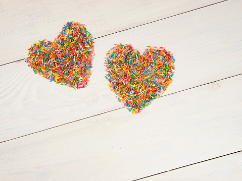 Candy sprinkles form heart shape. Multicolored heart-shape from candy confetti on white wooden background. Valentines day concept. Top view or flat lay with copyspace.