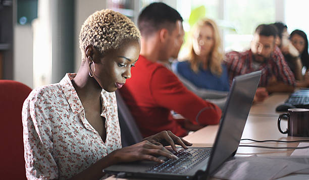 Application developers at work. Closeup side view of group of software developers working late at IT office. There is African american woman with short blond hair in focus, her colleagues in background, blurry. man and machine stock pictures, royalty-free photos & images