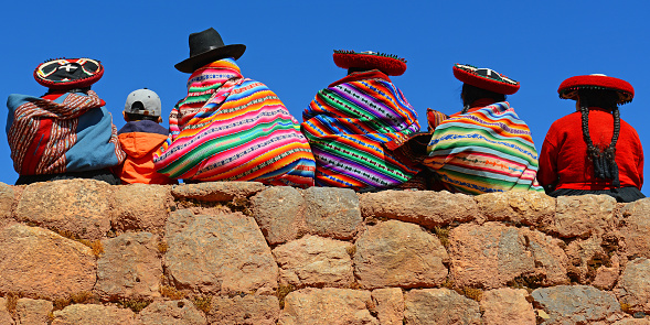 Chincheros, Peru - June 23, 2013: Quechua ladies with colorful textiles and hats sitting on an ancient Inca Wall together with a young boy with modern clothing.