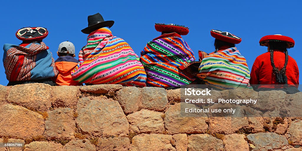 Quechua Indigenous Chincheros, Peru - June 23, 2013: Quechua ladies with colorful textiles and hats sitting on an ancient Inca Wall together with a young boy with modern clothing. Peru Stock Photo