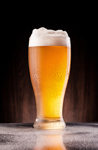 light cold beer in frosty glass over dark wooden background