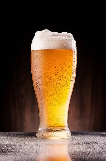 Photo of light beer in frosty glass over dark wooden background