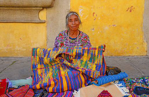 Antigua, Guatemala - March 28, 2013: A Maya saleswomen is showing her textiles in the local arts and crafts market in the main street of the city.