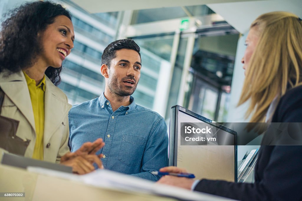 Un couple parle à un caissier de banque - Photo de Guichetier de banque libre de droits