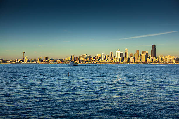 Downtown Seattle skyline as seen from across the water. The Space Needle can be seen off to the left of the frame. A boat is heading across the water towards the camera.