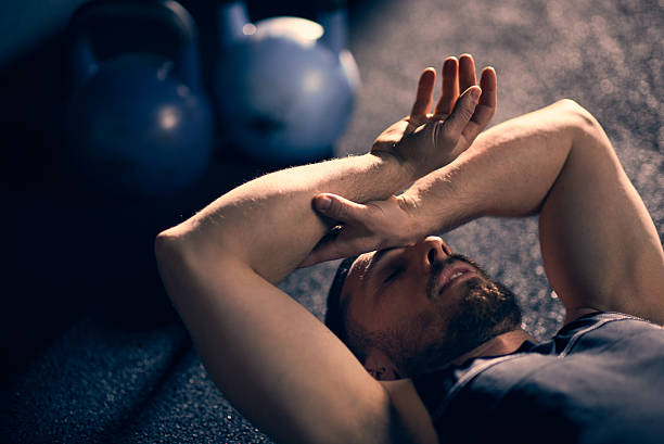 Tired athlete lying down with hand on his head at gym