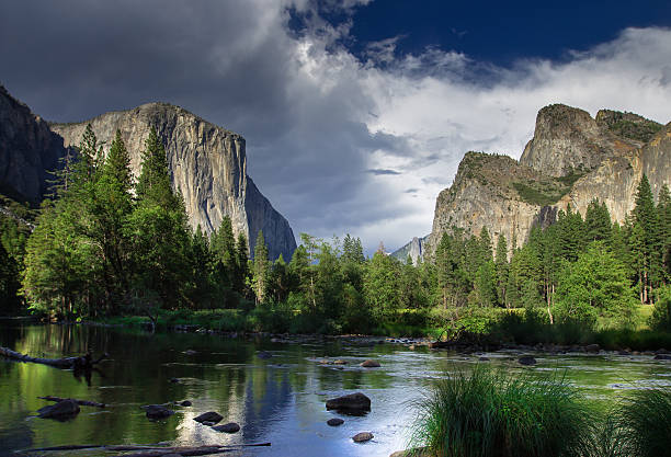 A thick sheet of gray cloud rolling over the granite formations of El Capitan and the Three Brothers, seen from the  floor of Yosemite Valley on the banks of the Merced River. Still taken from time lapse video #610816938.