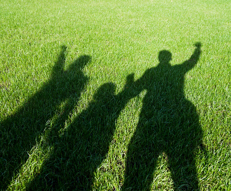 Shadows on the lawn of a family holding hands.