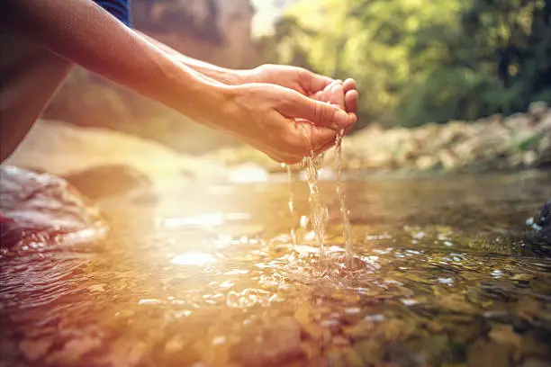 Human hand cupped to catch the fresh water from the river, reflection on water surface.