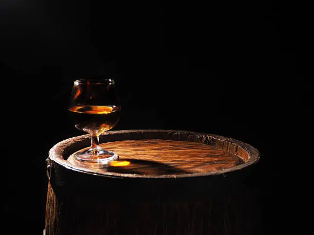 Glass of cognac with barrel on wooden backgroun.