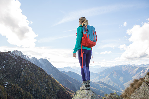 Young woman hiking reaches the mountain top, contemplates the beautiful view.