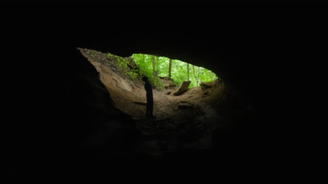 Caver Walks Towards Cave Entrance and Looks Upwards at the Rock - 4K
