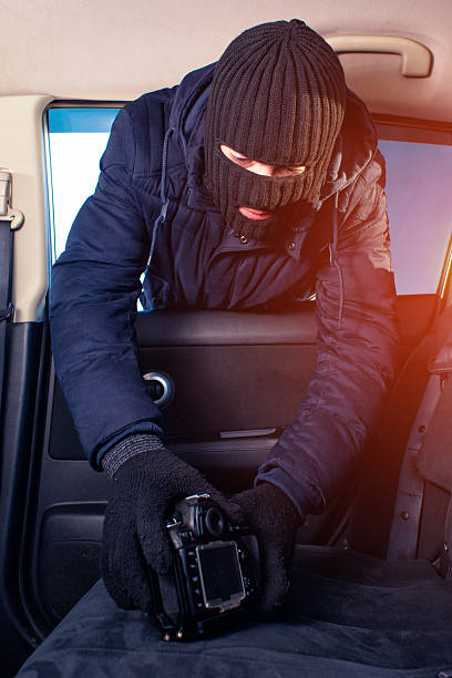 istock Male thief in mask stealing photo camera from car 638093126