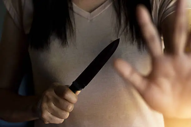 Woman holding a knife in hand while defending herself from attacks.