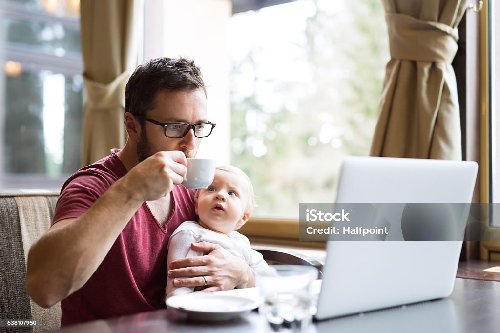 Man with notebook in cafe drinking coffee, holding his son Young handsome man with notebook in cafe sitting at the table drinking coffee, holding his son in his lap Father Stock Photo