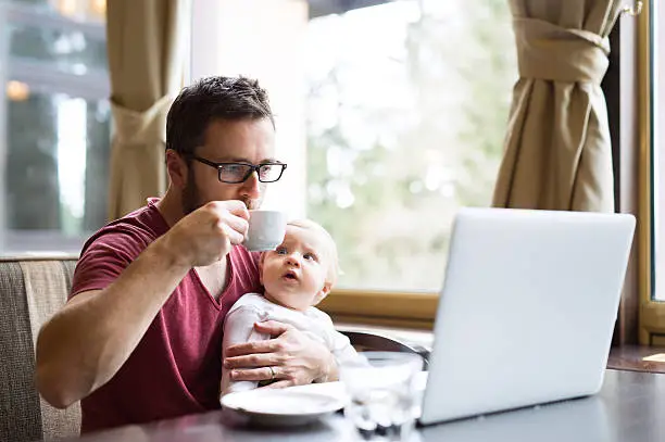 Photo of Man with notebook in cafe drinking coffee, holding his son