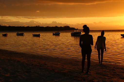 Albion, Mauritius - December 4, 2016: Girls enjoy the beautiful sunset at the beach of Albion. They take pictures with their smartphone.