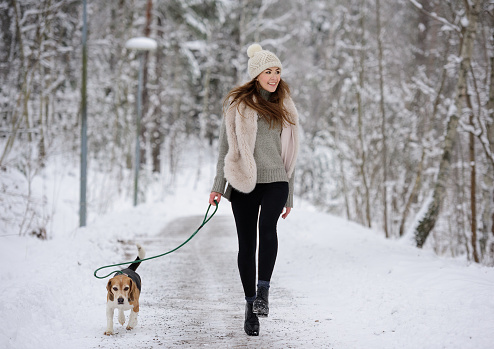 Happy woman running with beagle dog on winter walk path