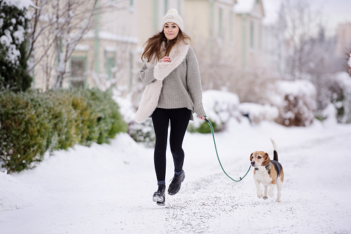 Happy woman running with beagle dog on winter street