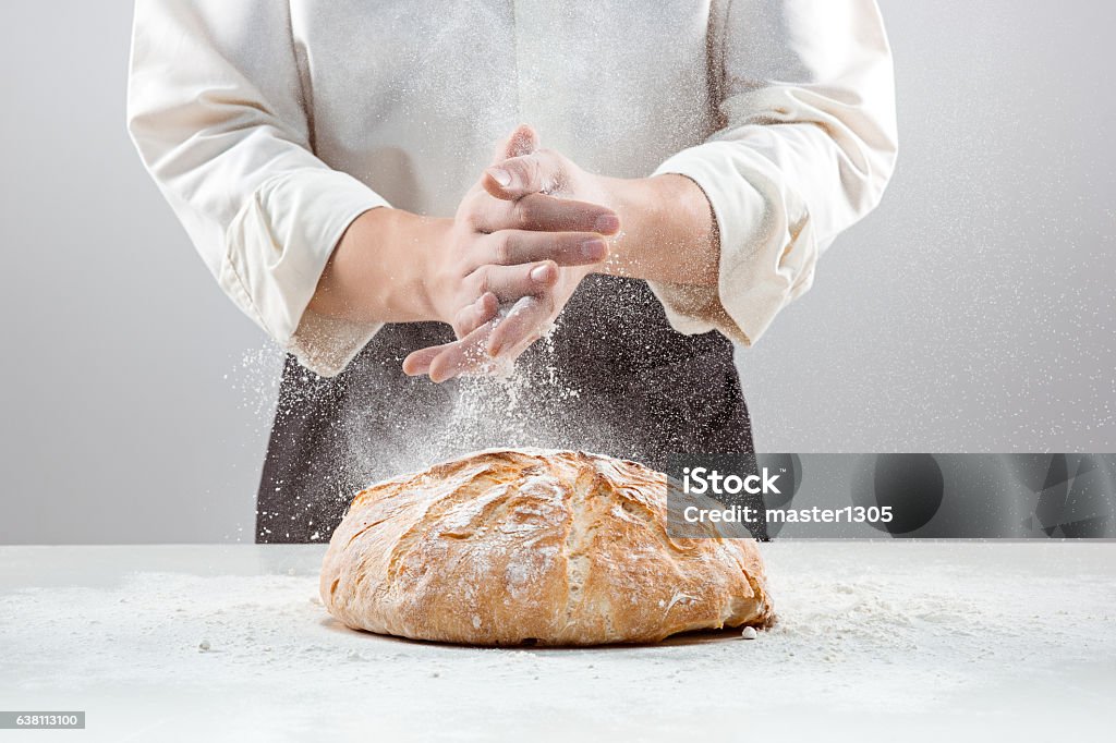 The male hands in flour and rustic organic loaf of The hands of baker man and rustic organic loaf of bread - rural bakery on gray Bakery Stock Photo