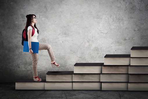Image of a female college student walking upward on the books stair. Concept of study hard