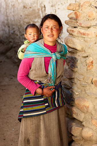 Tibetan woman carrying her baby, Upper Mustang. Mustang region is the former Kingdom of Lo and now part of Nepal,  in the north-central part of that country, bordering the People's Republic of China on the Tibetan plateau between the Nepalese provinces of Dolpo and Manang. The Kingdom of Lo, the traditional Mustang region, and “Upper Mustang” are one and the same, comprising the northern two-thirds of the present-day Nepalese Mustang District, and are well marked by official “Mustang” border signs just north of Kagbeni where a police post checks permits for non-Nepalese seeking to enter the region, and at Gyu La (pass) east of Kagbeni.http://bhphoto.pl/IS/mustang_380.jpg