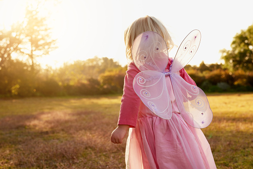 Rear view shot of a little girl dressed up as a fairy enjoying the day outside