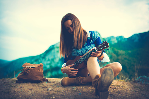 Hippie playing ukulele on top of the mountain.