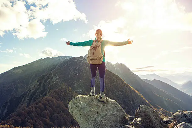 Photo of Young woman hiking reaches the mountain top, outstretches arms