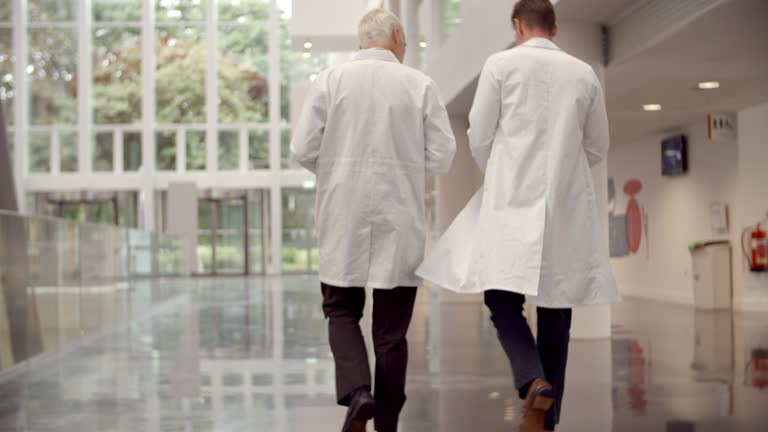 Rear View Of Doctors Talking As They Walk Through Hospital