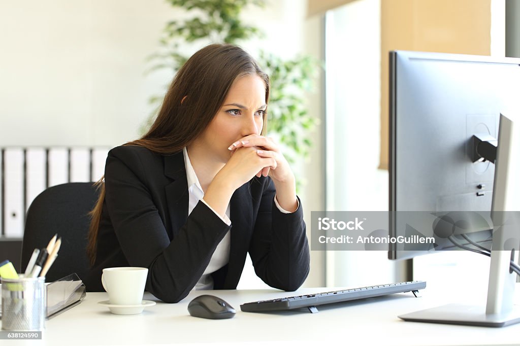 Businesswoman solving a difficult assignment Concentrated businesswoman trying to solve a difficult assignment on line in a desktop computer at office Suspicion Stock Photo