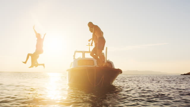 SLO MO Couple and their friends jumping off a boat at sunset